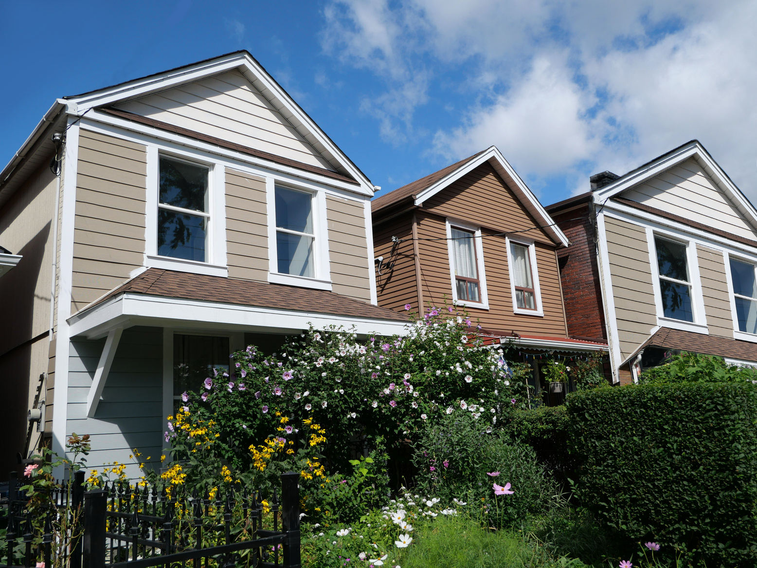Row of modest clapboard houses with gables and summer flowers in front garden